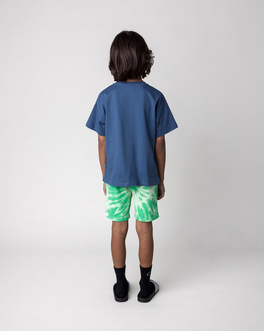 Kid wearing the Cool Crew Tee in blue with the Splatter Short in green, back view