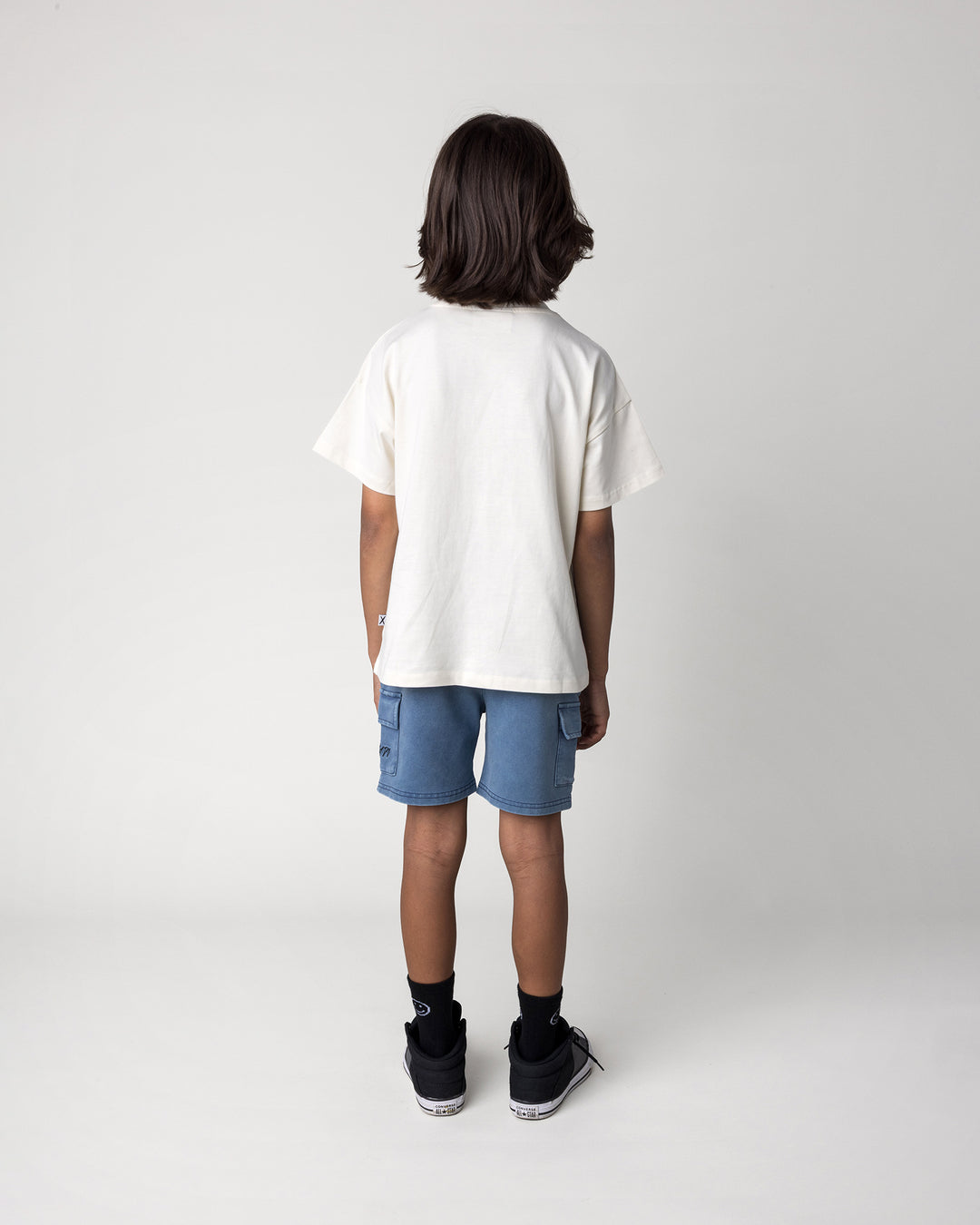 Kid wearing the Cool Crew Tee in cream with the Blasted Deluxe Cargo Short in midnight wash, back view