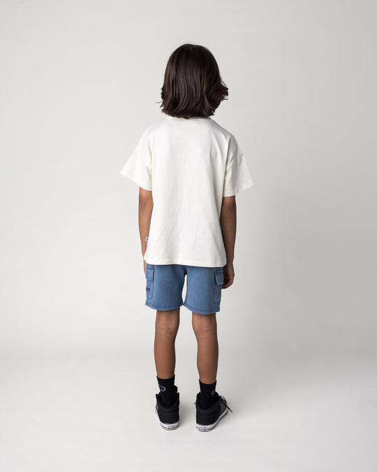 Kid wearing the Cool Crew Tee in cream with the Blasted Deluxe Cargo Short in midnight wash, back view