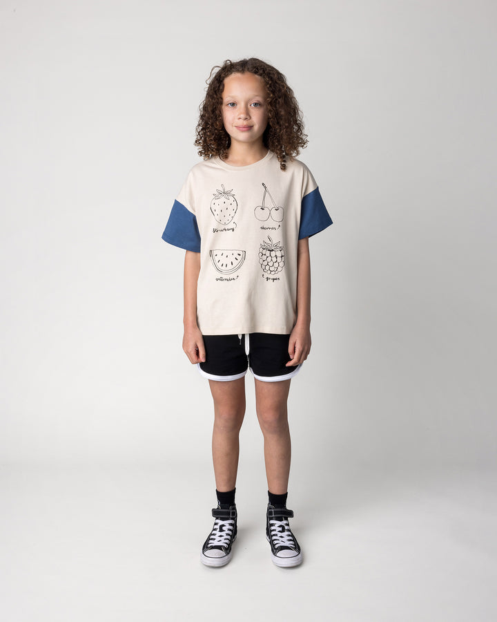 Kid wearing the Different Fruits Tee in stone and midnight with the Sprint Short in black and white, front view