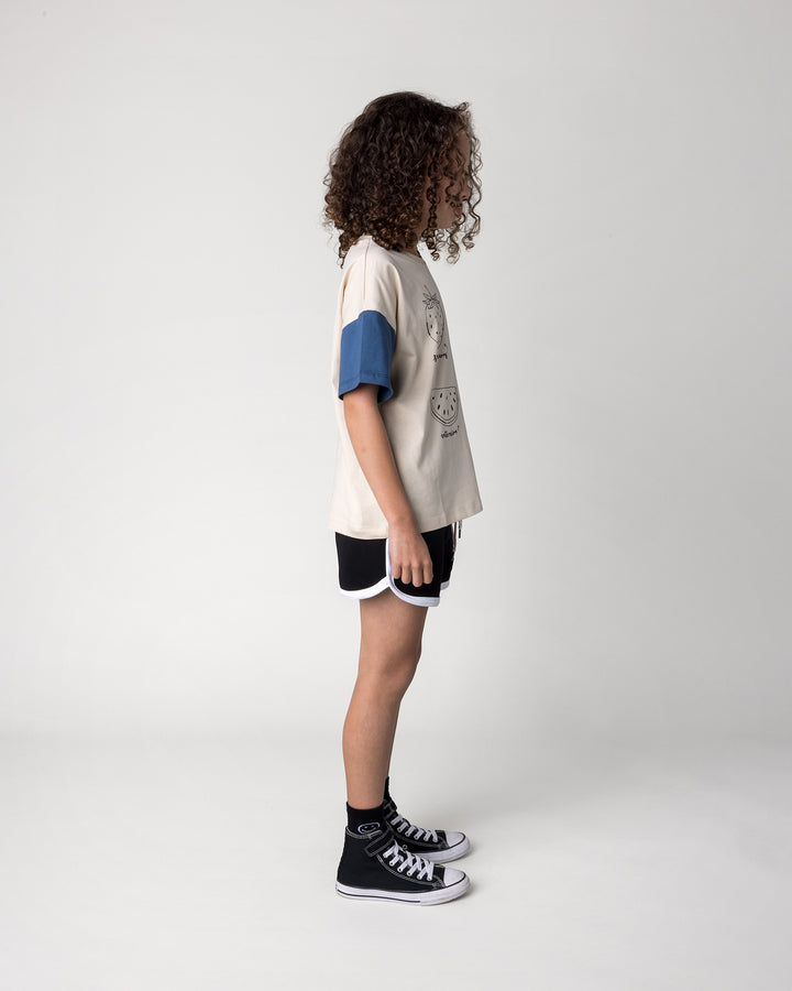 Kid wearing the Different Fruits Tee in stone and midnight with the Sprint Short in black and white, side view