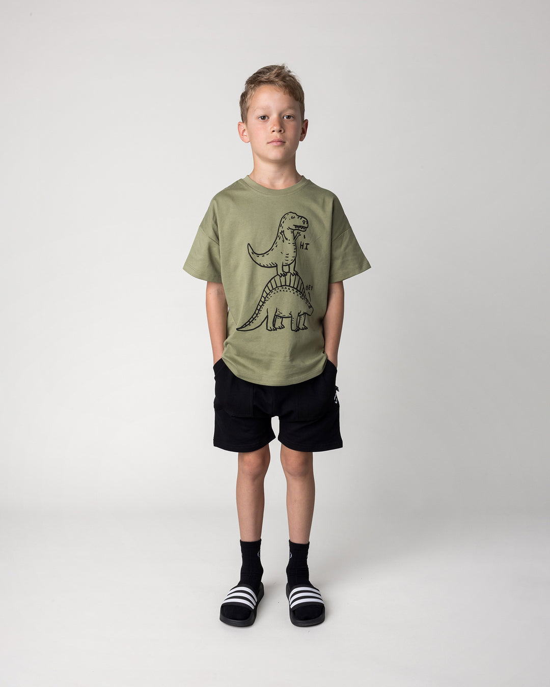 Kid wearing the Dino Ride Tee in light khaki with the Rib Pocket Short in black, front view