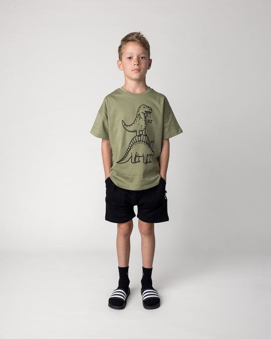 Kid wearing the Dino Ride Tee in light khaki with the Rib Pocket Short in black, front view