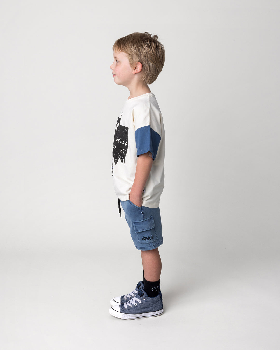 Kid wearing the Greetings Bat Tee in cream, black and midnight with the Blasted Deluxe Cargo Short in midnight wash, side view