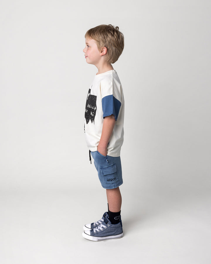 Kid wearing the Greetings Bat Tee in cream, black and midnight with the Blasted Deluxe Cargo Short in midnight wash, side view