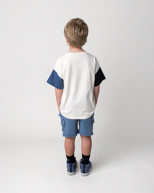 Kid wearing the Greetings Bat Tee in cream, black and midnight with the Blasted Deluxe Cargo Short in midnight wash, back view