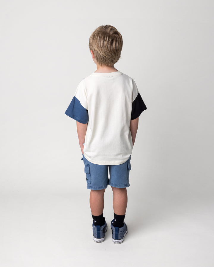 Kid wearing the Greetings Bat Tee in cream, black and midnight with the Blasted Deluxe Cargo Short in midnight wash, back view