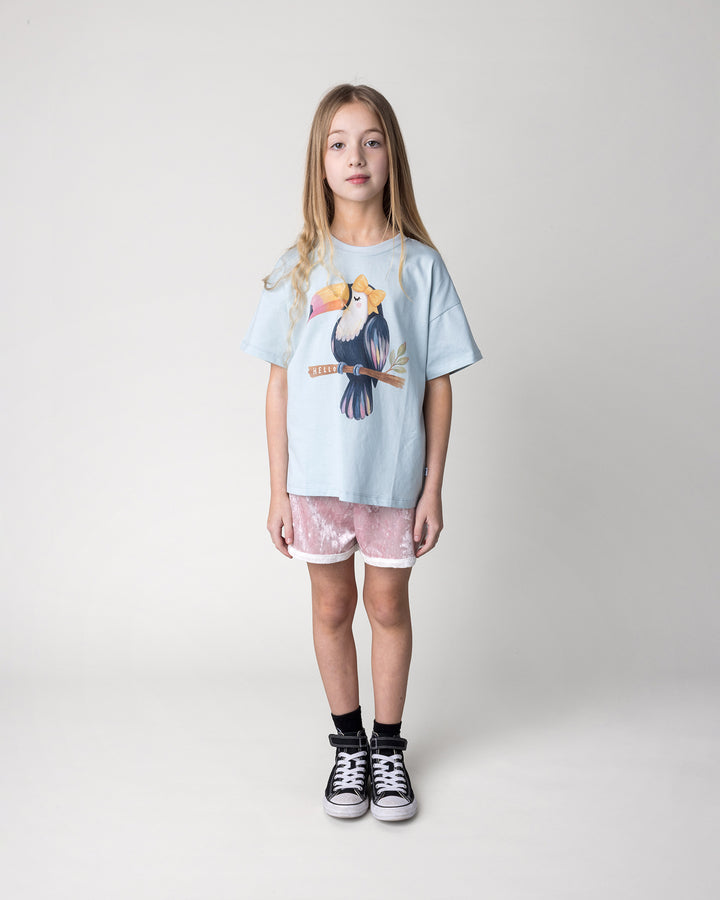 Kid wearing the Hello Toucan Tee in light blue with the Velvet Runner Short in blush and cream, front view