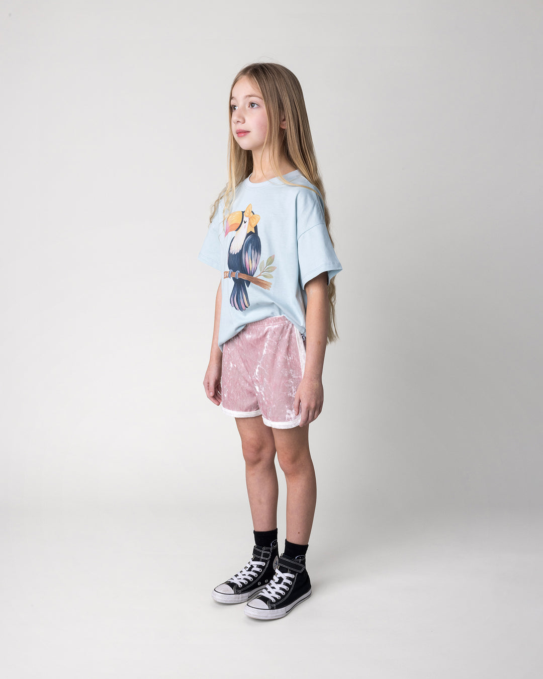 Kid wearing the Hello Toucan Tee in light blue with the Velvet Runner Short in blush and cream, side view