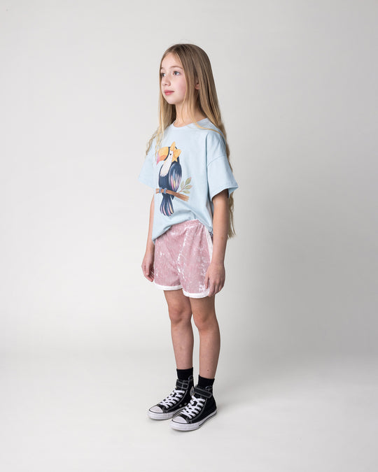 Kid wearing the Hello Toucan Tee in light blue with the Velvet Runner Short in blush and cream, side view