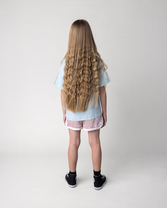 Kid wearing the Hello Toucan Tee in light blue with the Velvet Runner Short in blush and cream, back view
