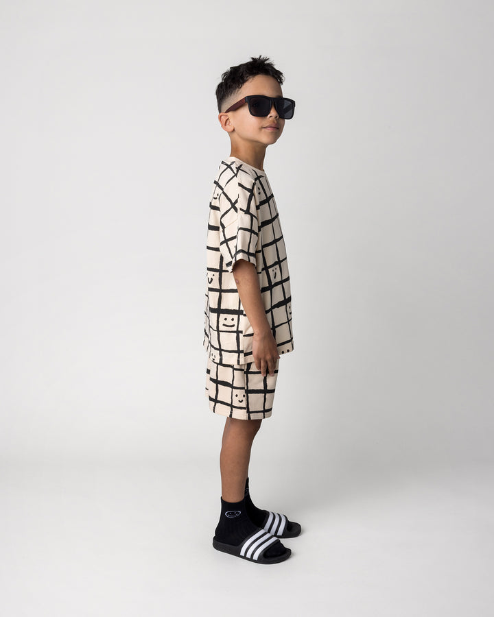 Kid wearing the Happy Squares Tee in beige with the Happy Squares Short in beige, side view