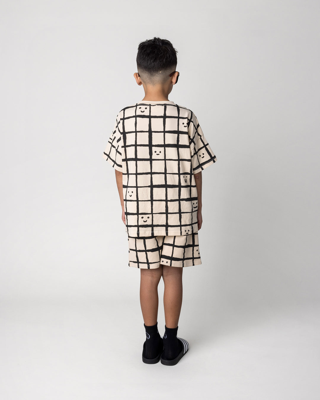 Kid wearing the Happy Squares Tee in beige with the Happy Squares Short in beige, back view