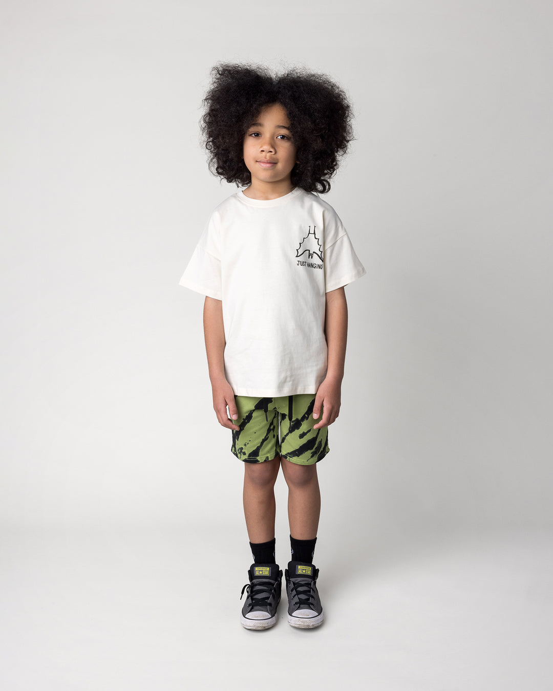 Kid wearing the Just Hanging Tee in cream with the Strike Short in lime, front view
