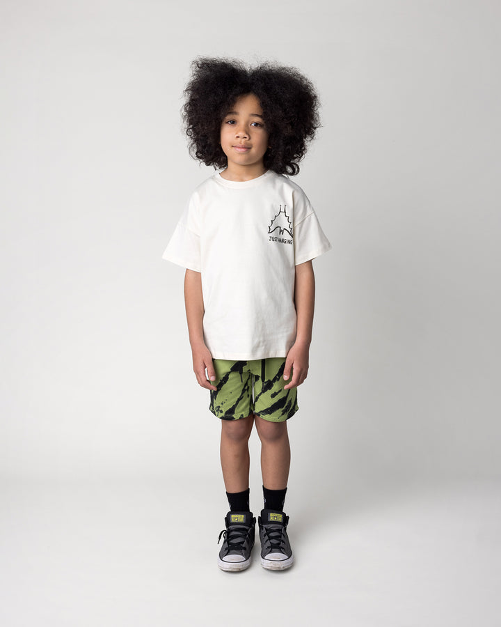 Kid wearing the Just Hanging Tee in cream with the Strike Short in lime, front view