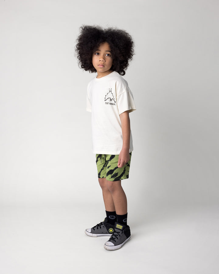 Kid wearing the Just Hanging Tee in cream with the Strike Short in lime, side view