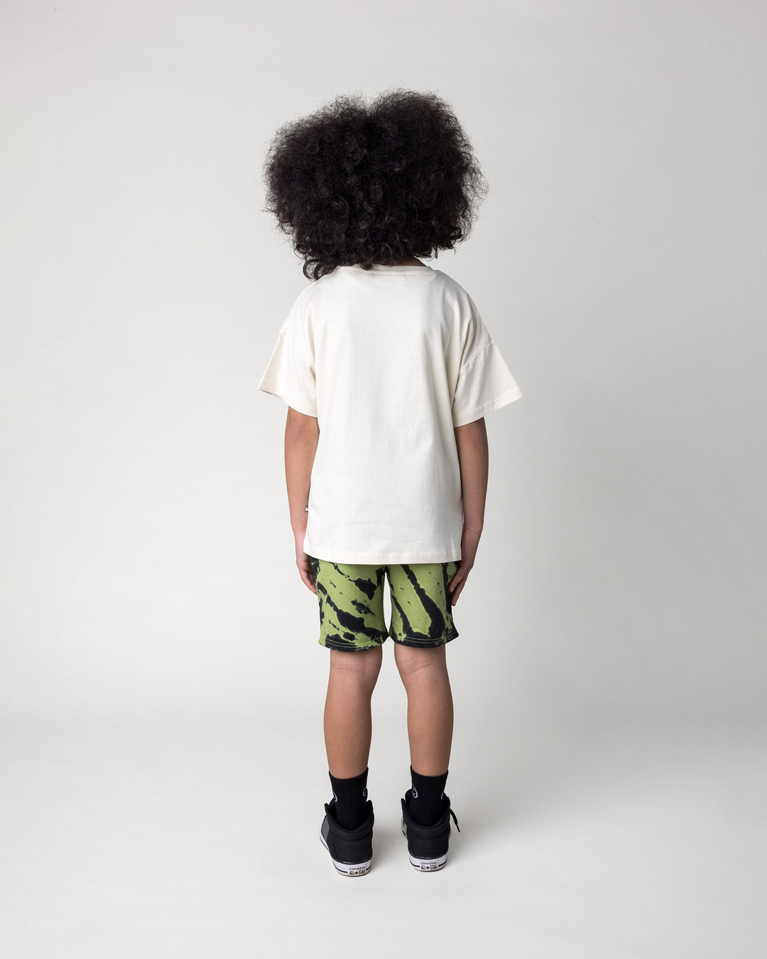 Kid wearing the Just Hanging Tee in cream with the Strike Short in lime, back view