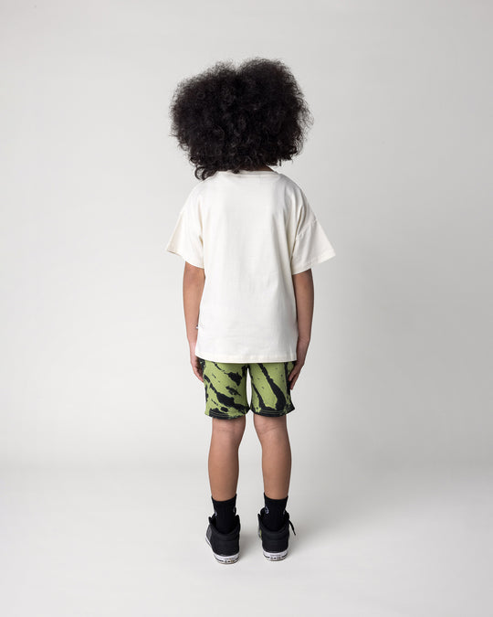 Kid wearing the Just Hanging Tee in cream with the Strike Short in lime, back view