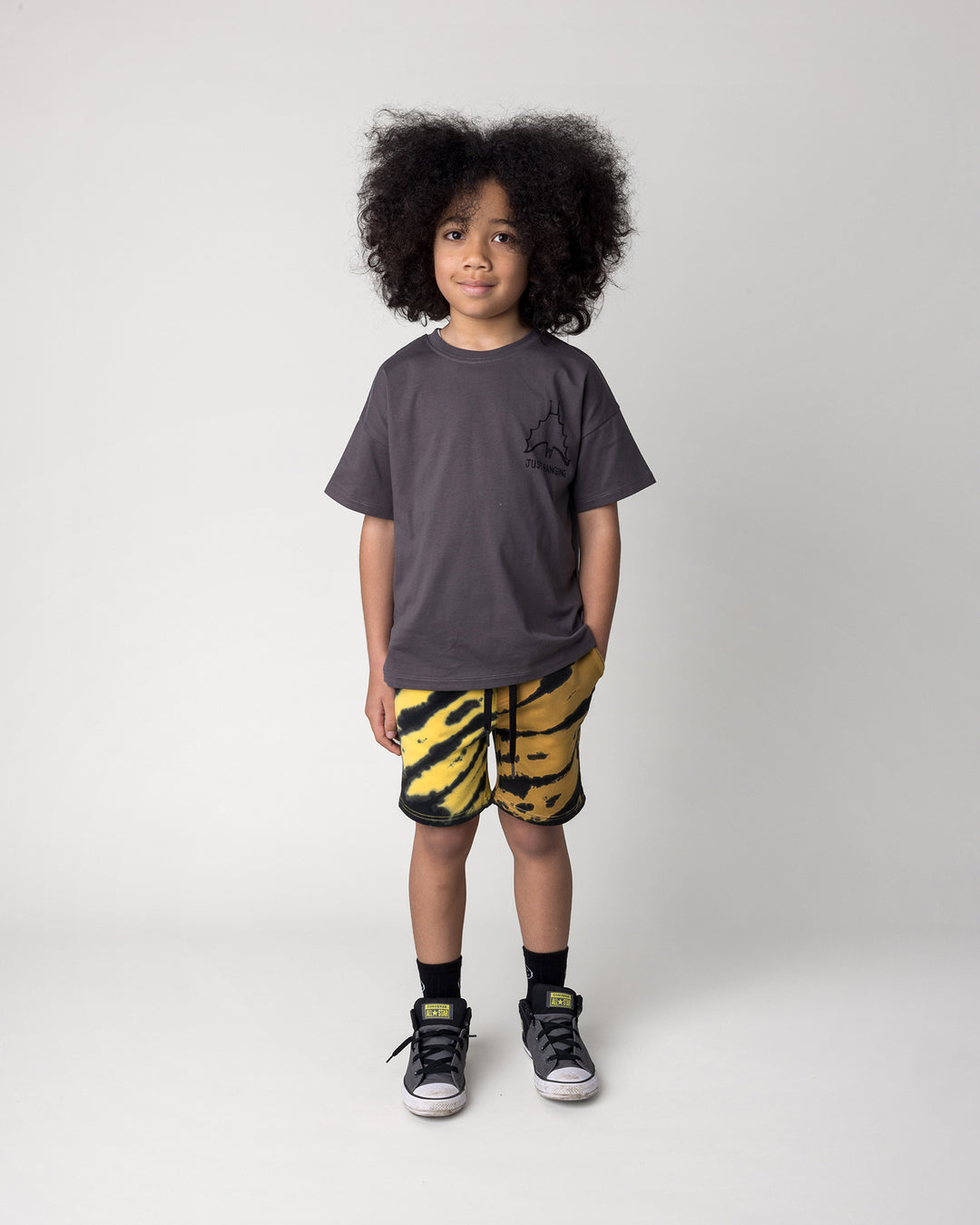 Kid wearing the Just Hanging Tee in dark grey with the Duo Tie Dye Short in lemon and rust, front view