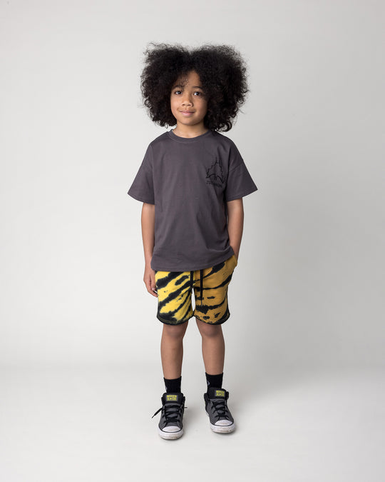 Kid wearing the Just Hanging Tee in dark grey with the Duo Tie Dye Short in lemon and rust, front view