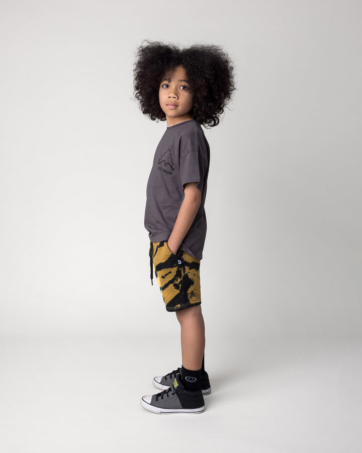 Kid wearing the Just Hanging Tee in dark grey with the Duo Tie Dye Short in lemon and rust, side view