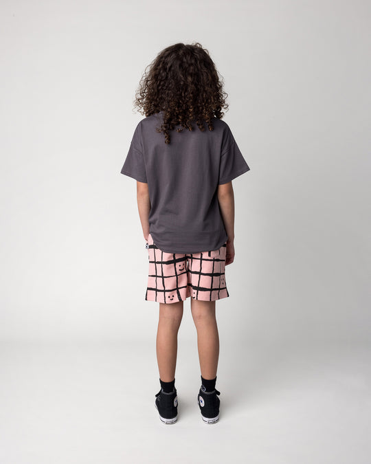 Kid wearing the Just Hanging Tee in dark grey with the Happy Squares Short in dusty pink, back view