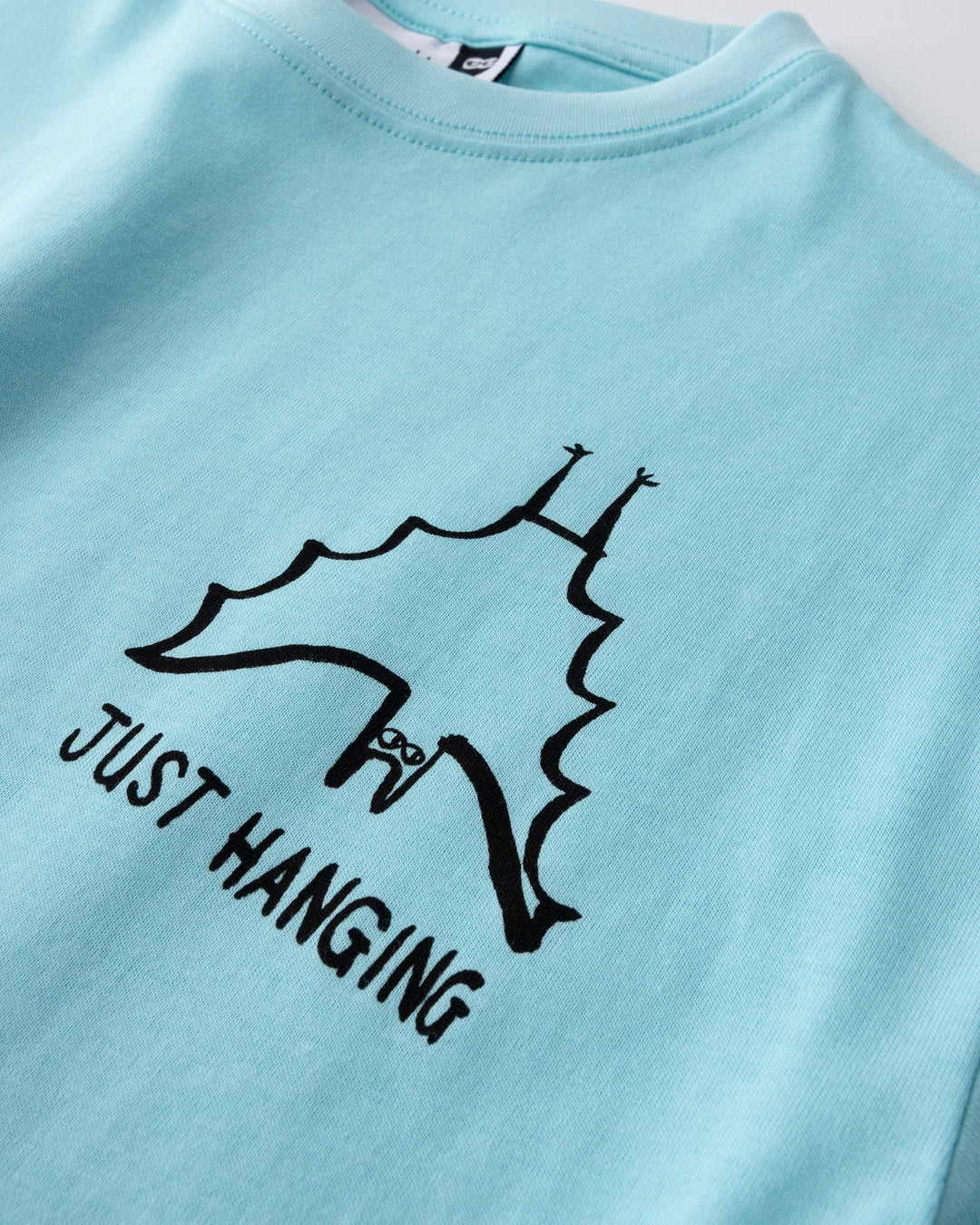 Close up of the Just Hanging Tee print in light aqua
