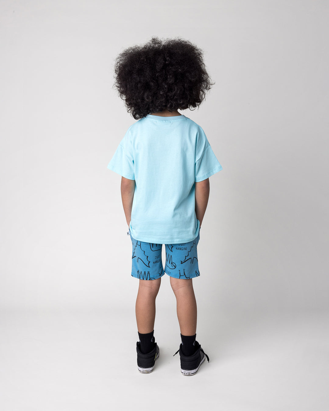 Kid wearing the Just Hanging Tee in light aqua with the Just Hanging Short in sky wash, back view