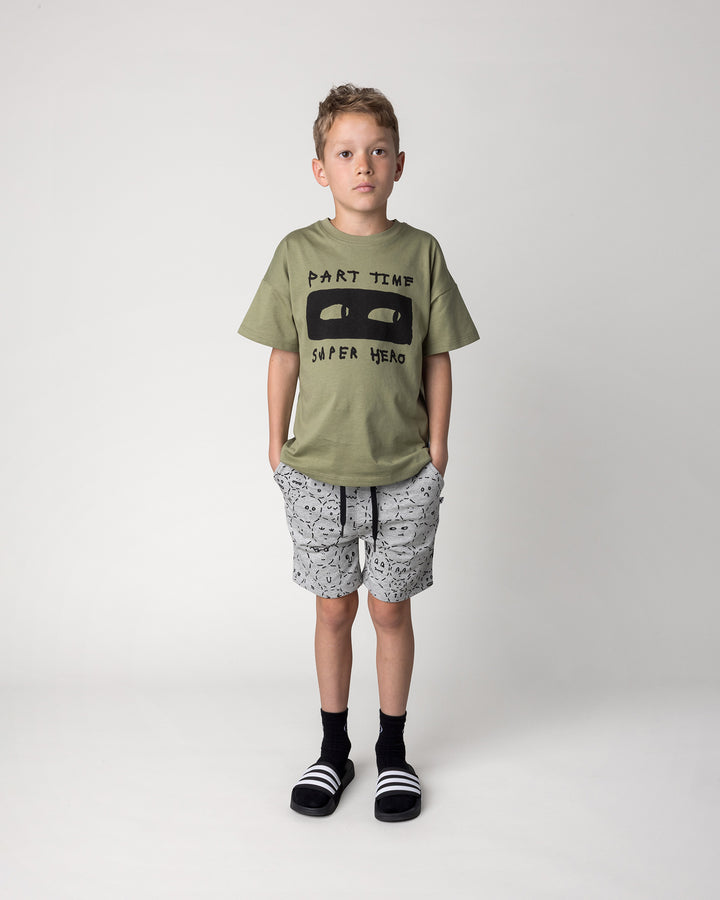 Kid wearing the Part Time Super Hero Tee in light khaki with the Different Faces Short in grey marle and black, front view