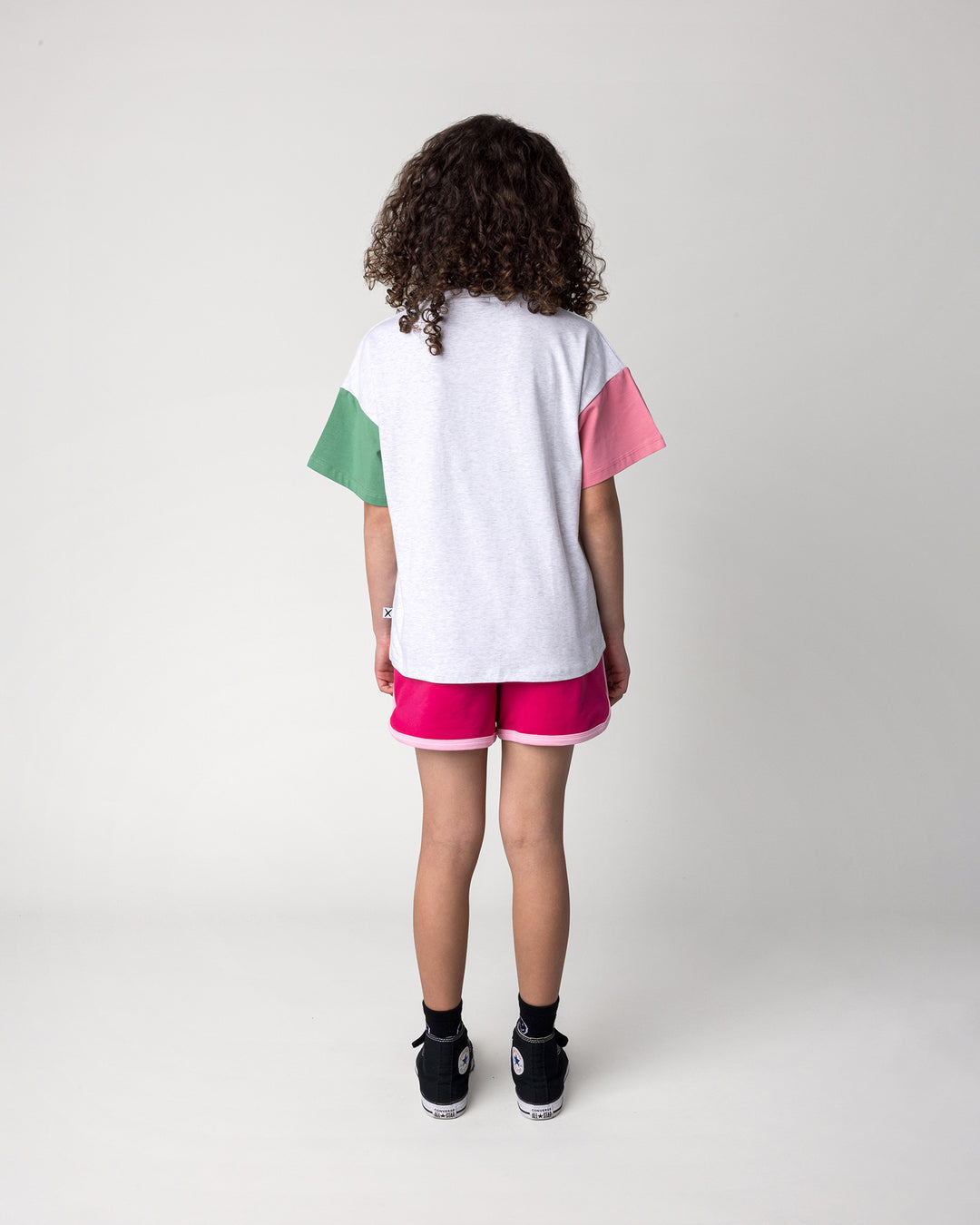 Kid wearing the Scooting Watermelon Tee in white marle, candy and green with the Sprint Short in crimson and pink, back view