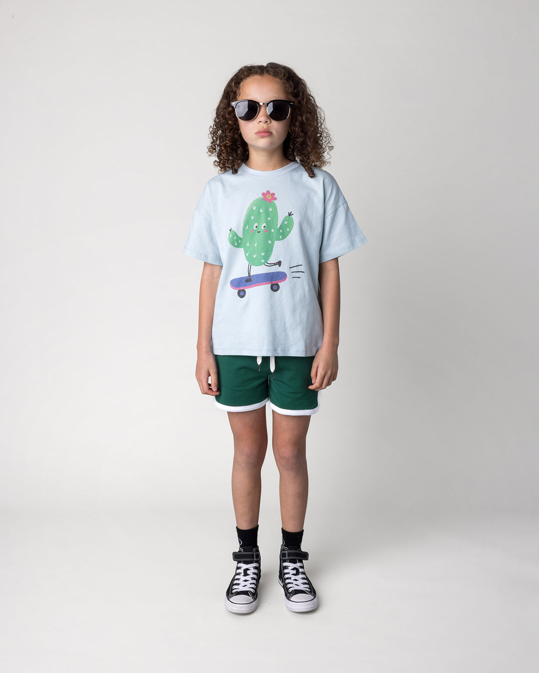 Kid wearing the Skate Cactus Tee in light blue with the Sprint Short in kelly green and white, front view