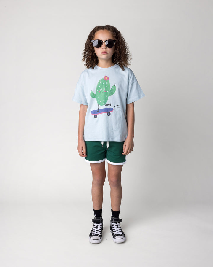 Kid wearing the Skate Cactus Tee in light blue with the Sprint Short in kelly green and white, front view