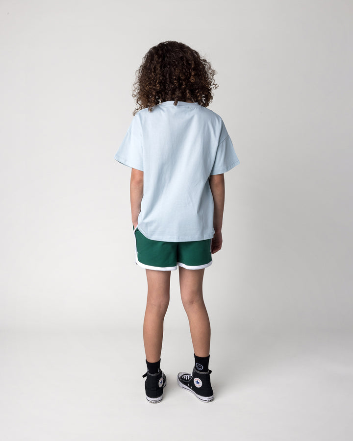 Kid wearing the Skate Cactus Tee in light blue with the Sprint Short in kelly green and white, back view