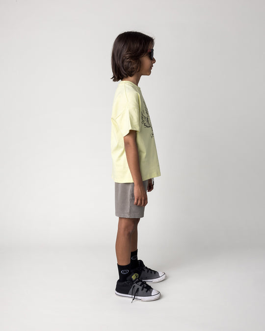 Kid wearing the Skate Phoenix Tee in light zest with the Blasted Track Short in grey wash, side view