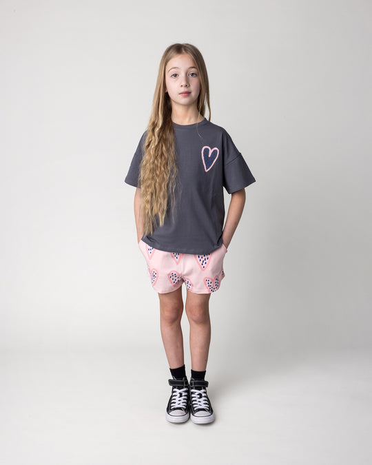 Kid wearing the Speckle Heart Tee in dark grey with the Speckle Heart Short in pink, front view