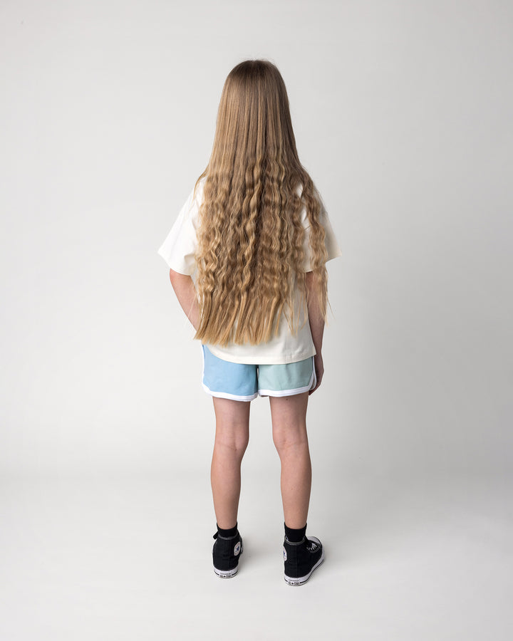 Kid wearing the Unicorn Club Tee in cream with the Sprint Short in mint, aqua and lilac, back view