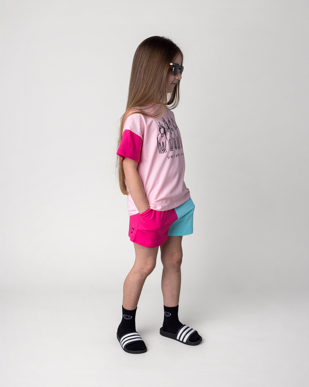 Kid wearing the Unicorn Club Tee in pink, hot pink and aqua with the Two Tone Short in hot pink and aqua, side view