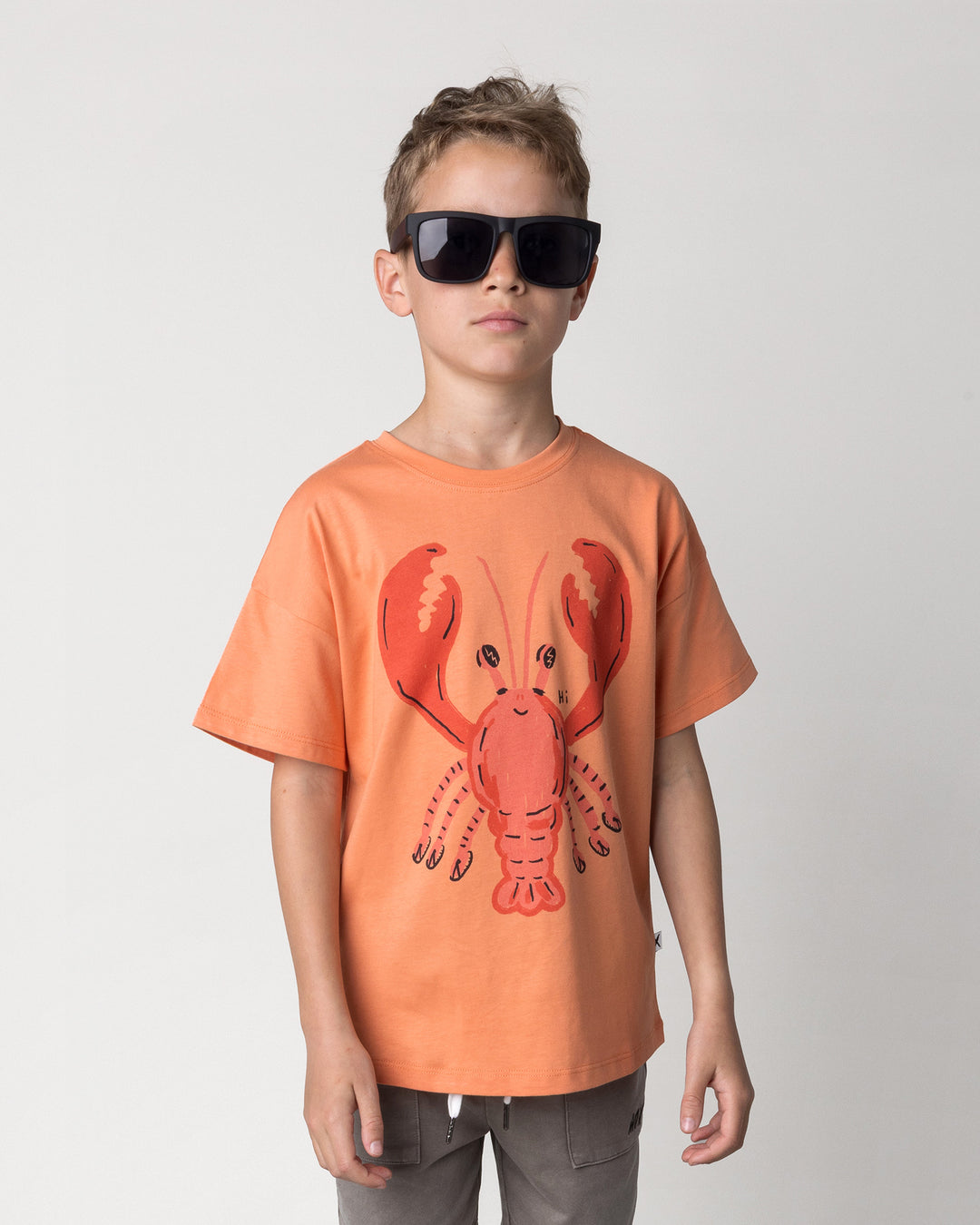 Close up of the Vacay Crayfish Tee in light orange on a kid, front view