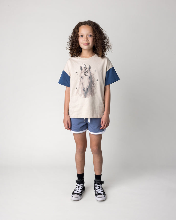 Kid wearing the Watercolour Unicorn Tee in stone and midnight with the Sprint Short in cornflower and white, front view