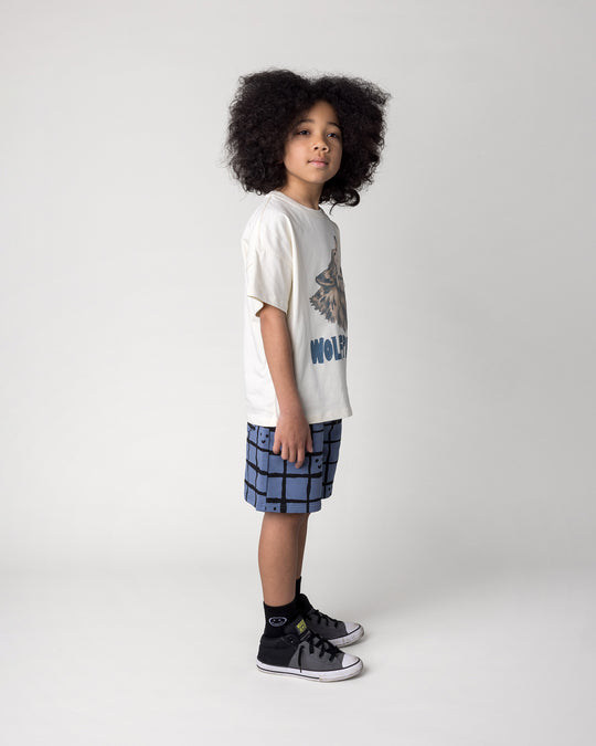 Kid wearing the Wolfpack Tee in cream with the Happy Squares Short in muted blue, side view