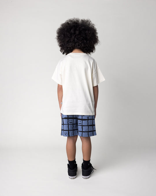 Kid wearing the Wolfpack Tee in cream with the Happy Squares Short in muted blue, back view
