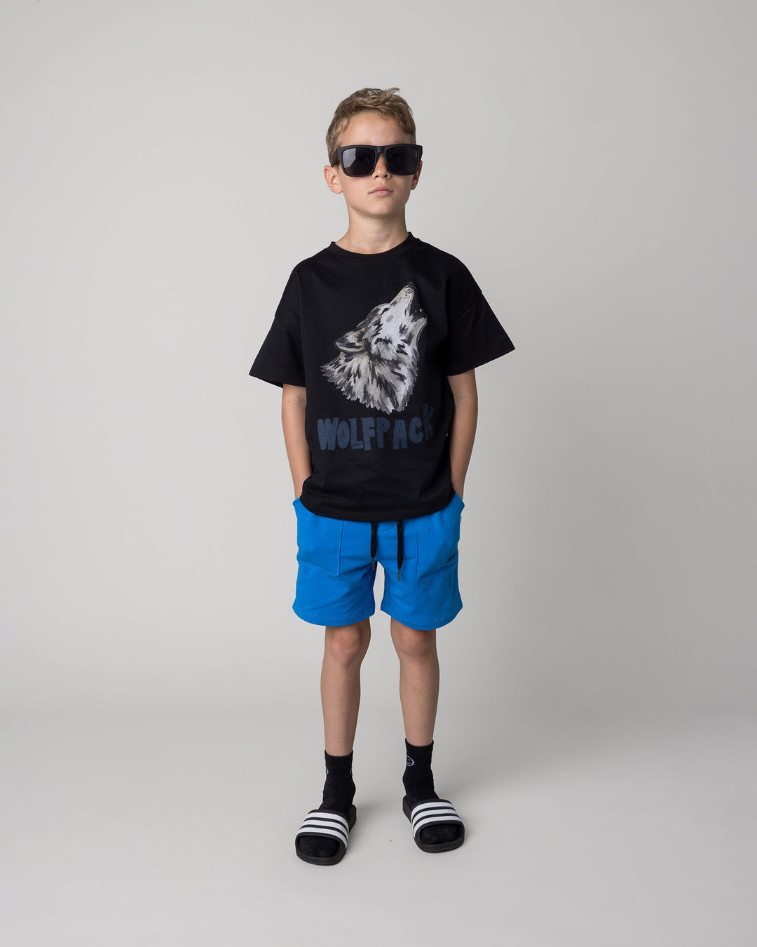Kid wearing the Track Short in cobalt with the Fast Panda Tee in white and orange, front view
