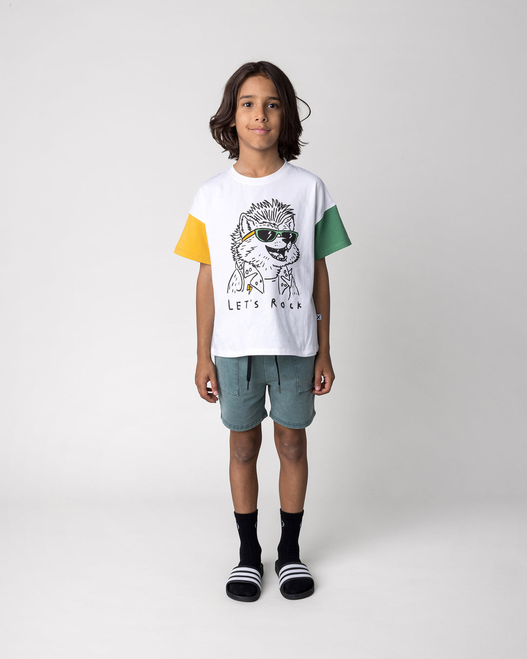 Kid wearing the Werewolf Rockstar Tee in off white, mustard and turf with the Blasted Track Short in forest wash, front view