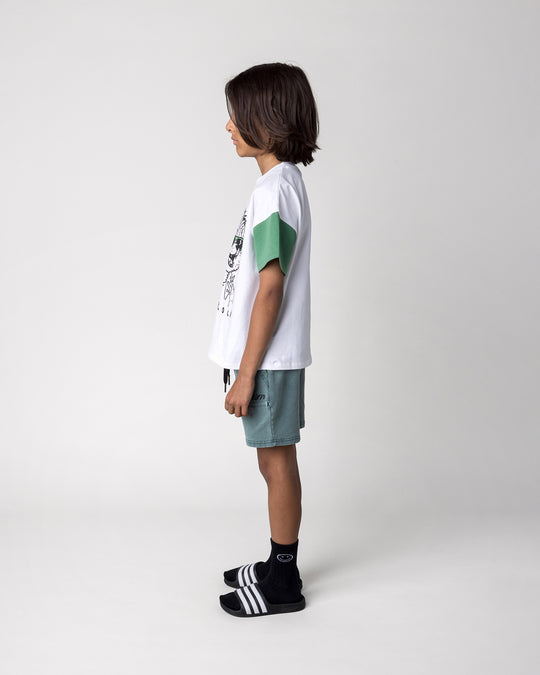 Kid wearing the Werewolf Rockstar Tee in off white, mustard and turf with the Blasted Track Short in forest wash, side view