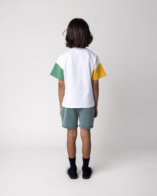 Kid wearing the Werewolf Rockstar Tee in off white, mustard and turf with the Blasted Track Short in forest wash, back view