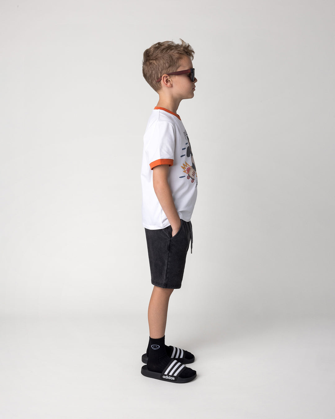 Kid wearing the Fast Panda Tee in white and orange with the Blasted Icon Short in black wash, side view