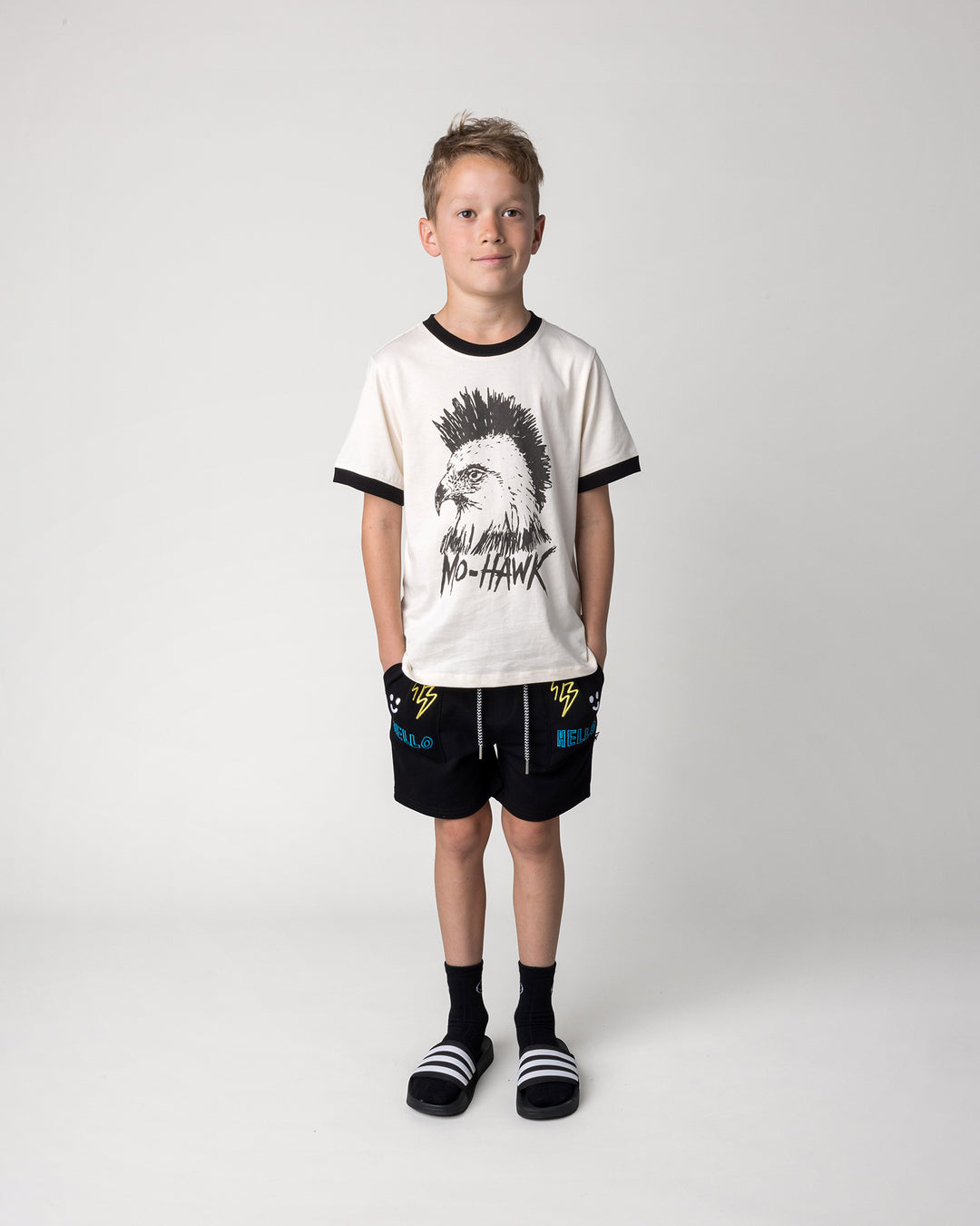 Kid wearing the Mo-Hawk Tee in cream and black with the Badges Short in black, front view