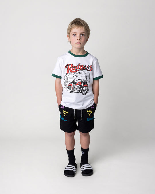 Kid wearing the Radness Tee in white and jungle with the Badges Short in black, front view