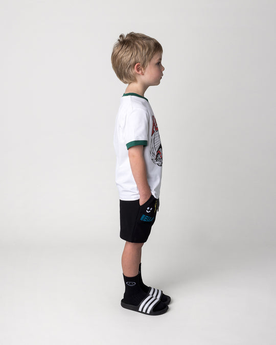 Kid wearing the Radness Tee in white and jungle with the Badges Short in black, side view