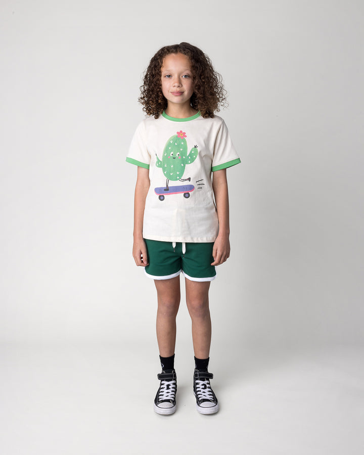 Kid wearing the Skate Cactus Tee in cream and green with the Sprint Short in kelly green and white, front view